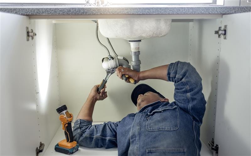 Plumber repairing pipes beneath a bathroom sink in Los Altos